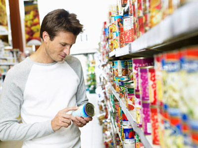 Man reading side of canned food in supermarket aisle