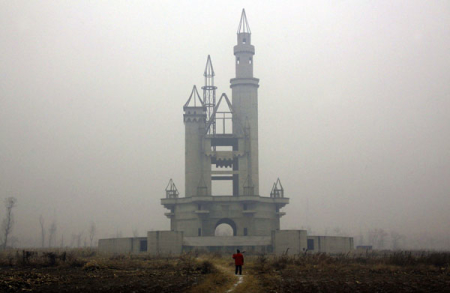 ATTENTION EDITORS -- THIS IMAGE IS 1 of 18 TO ACCOMPANY A PICTURE PACKAGE ON AN ABANDONED AMUSEMENT PARK NEAR BEIJING. SEARCH KEYWORD "WONDERLAND" TO SEE ALL IMAGES PXP201-218. A farmer carries a shovel over his shoulder as he walks to tend his crops in a field that includes an abandoned building, that was to be part of an amusement park called 'Wonderland', on the outskirts of Beijing December 5, 2011. Construction work at the park, which was promoted by developers as 'the largest amusement park in Asia', stopped around 1998 after funds were withdrawn due to disagreements over property prices with the local government and farmers. With local governments often dependent on land sales to fund payments on a staggering 10.7 trillion yuan ($1.7 trillion) of debt, Beijing worries that a collapsing property market will trigger a wave of defaults that in turn will hit the banks. More worrisome, the property market, which contributes about 10 percent of Chinese growth and drives activity in 50 other sectors, could drag the real economy to a hard landing. Picture taken December 5, 2011. REUTERS/David Gray (CHINA - Tags: REAL ESTATE BUSINESS SOCIETY CONSTRUCTION)